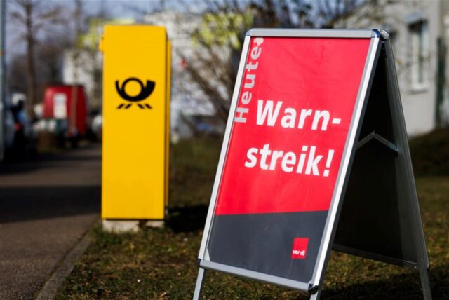 Ein Aufsteller mit der Aufschrift „Heute Warnstreik!“ steht neben einem Briefkasten der Deutschen Post.