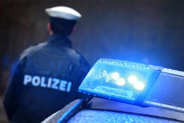 Ein Polizist steht neben einem Streifenwagen.