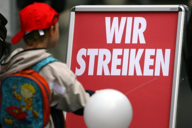 Ein Kita-Kind geht an einem roten Schild mit der Aufschrift „Wir Streiken“ vorbei.
