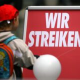 Ein Kita-Kind geht an einem roten Schild mit der Aufschrift „Wir Streiken“ vorbei.