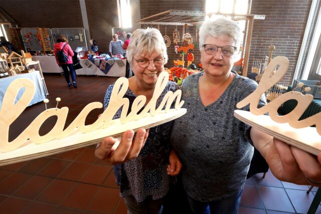 Roswitha Lotz und Martina Dudek (r.) halten beim Kreativmarkt „Holzwickeder Frühling“ gefräste Holzarbeiten in die Kamera