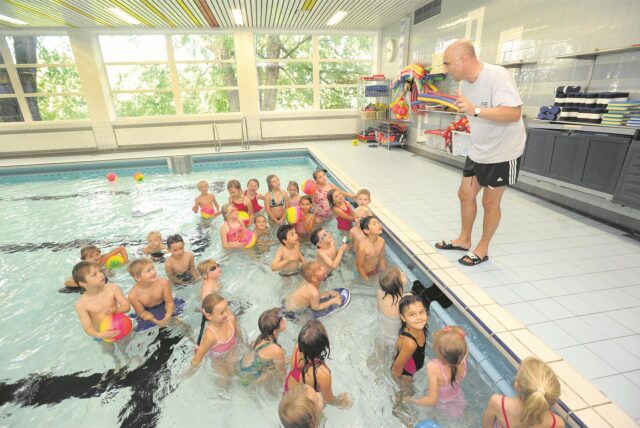 Im Becken des Massener Hellweg-Schwimmbades lauscht eine Schulklasse den Ausführungen ihres Lehrers Matthias Landsberg, der vom Beckenrand aus spricht.