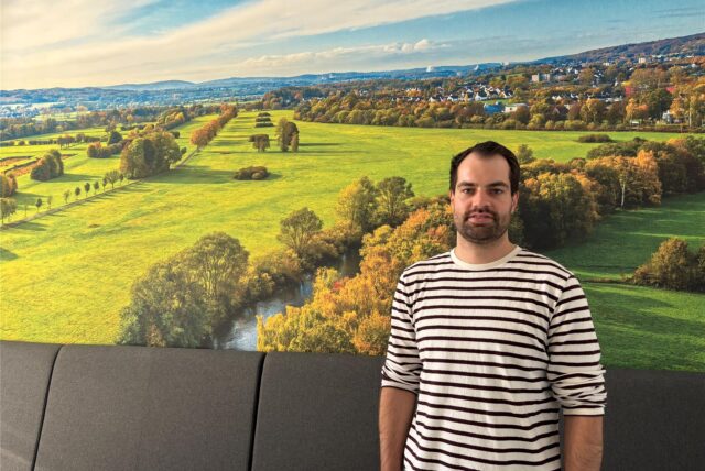 Florian Hübner, Umwelt- und Klimaschutzbeauftragter bei der Stadt Schwerte, steht vor einem Bild, das die Ruhrwiesen zeigt.