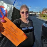 Neben einem Auto, das auf der Straße vor ihrer Tür parkt, zeigt Anwohnerin Iris Bolte einen auf orangefarbenem Papier gedruckten Warnhinweis der Stadt Unna. Autofahrer werden darauf hingewiesen, dass sie künftig mit Knöllchen zu rechnen hätten.