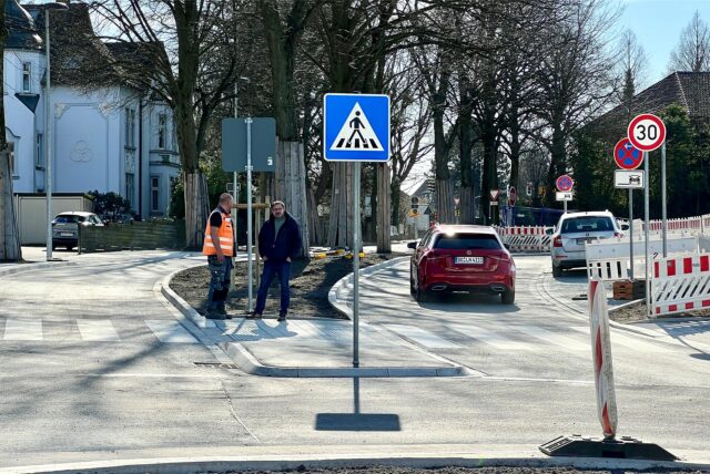 Zwei Männer stehen auf der Mittelinsel der neu gebauten Hertingerstraße. Ein Auto fährt an ihnen vorbei