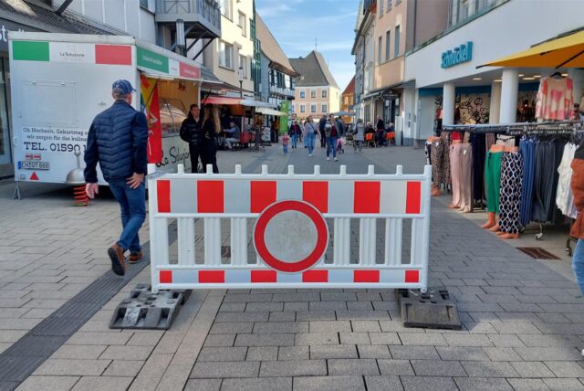 Auf der Massener Straße in Unnas Fußgängerzone steht eine rot-weiße Kunststoffabsperrung mit einem Durchfahrt-verboten-Schild. Dahinter beginnt der Aufstellbereich des Wochenmarktes.