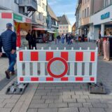 Auf der Massener Straße in Unnas Fußgängerzone steht eine rot-weiße Kunststoffabsperrung mit einem Durchfahrt-verboten-Schild. Dahinter beginnt der Aufstellbereich des Wochenmarktes.
