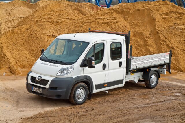 Ein weißer Peugeot Boxer Pritschenwagen steht vor einem großen Berg Sand, den es zu verladen gilt.