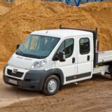 Ein weißer Peugeot Boxer Pritschenwagen steht vor einem großen Berg Sand, den es zu verladen gilt.