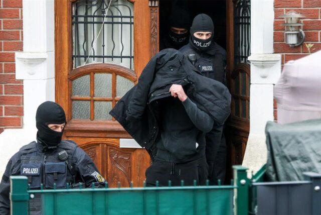 Polizeibeamte führen einen Tatverdächtigen aus einem durchsuchten Haus.