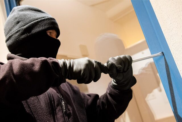Ein in schwarz vermummter Mann versucht, mit einem Brecheisen ein Fenster aufzuhebeln.