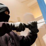 Ein in schwarz vermummter Mann versucht, mit einem Brecheisen ein Fenster aufzuhebeln.
