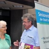 Ein Seniorenbeirats-Vertreter im Gespräch mit einer Seniorin neben einem Transparent des Seniorenbeirats.