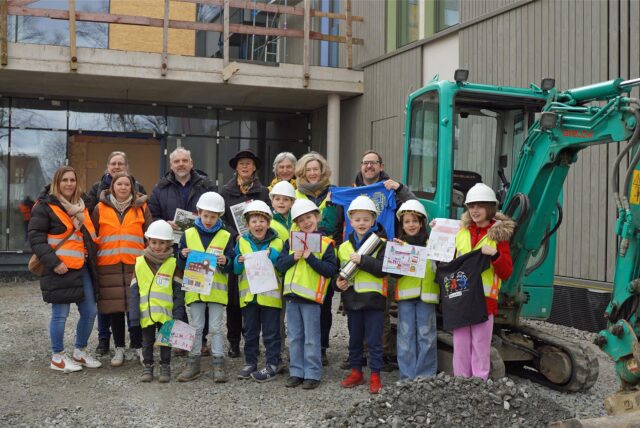 Kinder aus Unna stehen mit Baustellenhelm und Signalweste auf der Baustelle des neuen Bildungszentrums am Hertinger Tor, wo sie eine Zeitkapsel befüllt haben.