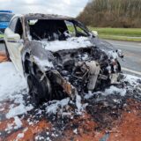 Ein ausgebranntes weißes Auto steht an der Autobahnabfahrt Kamen/Bergkamen. Dahinter ist ein Polizeiwagen zu sehen.