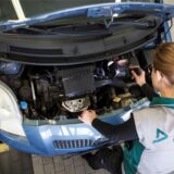Eine Prüferin der Dekra beugt sich über den geöffneten Motorraum eines blauen Toyota Yaris.