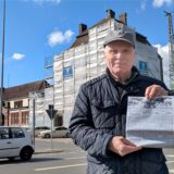 Ein Mann steht mit einer historischen Ausgabe der Schwerter Zeitung vor dem eingerüsteten Bahnhofsgebäude in Schwerte.