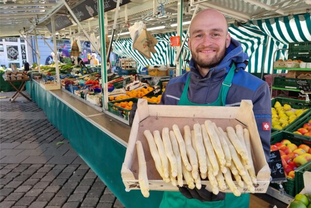 Der Inhaber eines Obst- und Gemüsestands am Wochenmarkt in Unna, Laslo Wucherpfennig, hält eine Kiste Spargel in die Kamera.