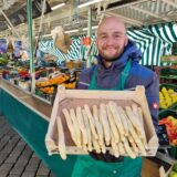 Der Inhaber eines Obst- und Gemüsestands am Wochenmarkt in Unna, Laslo Wucherpfennig, hält eine Kiste Spargel in die Kamera.