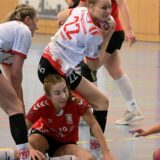 Nele Wagener vom HC Tura Bergkamen fängt einen Ball ab. Carla Verhasselt und Thia-Carolin Schmidt vom Lüner SV Handball sitzen auf dem Boden.