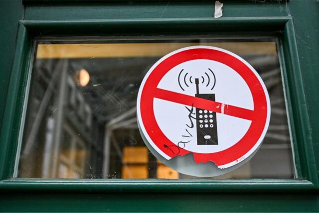 Ein Schild mit einem durchgestrichenen Handy-Symbol weist in einer Schule auf ein Handyverbot hin.