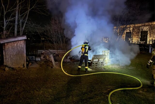 Ein Feuerwehrmann löscht einen Bereich im Freien bei starker Rauchentwicklung.