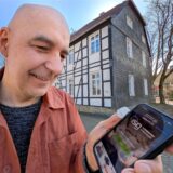 Holger Ehrich, Leiter des Kulturbüros in Schwerte, steht mit einem Smartphone in der Hand vor dem Wuckenhof.