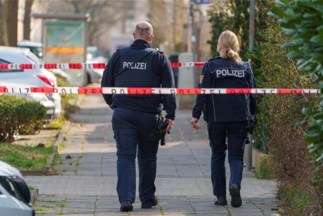 Eine Crimescene: Zwei Polizisten laufen durch einen abgesperrten Tatort.