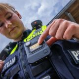 Eine Polizistin schaltet die Bodycam an ihrer Uniform an.