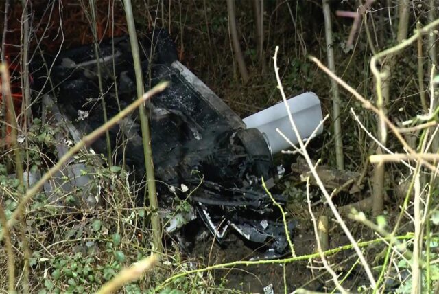 Nach einem Unfall liegt ein silberner PKW in einer Böschung auf dem Dach.