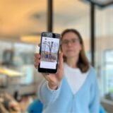 Eine Frau hält ein Handy, auf dem der WhatsApp-Kanal der Feuerwehr Kamen zu sehen ist, in die Kamera