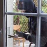 Ein in Schwarz gekleideter und vermummter Mann stemmt eine Balkontür mit einem Brecheisen auf.