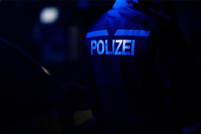 Ein Polizist in der Dunkelheit, auf seiner Jacke ist das Wort „Polizei“ in hellen Buchstaben zu erkennen.