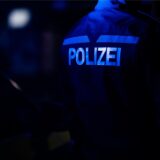Ein Polizist in der Dunkelheit, auf seiner Jacke ist das Wort „Polizei“ in hellen Buchstaben zu erkennen.