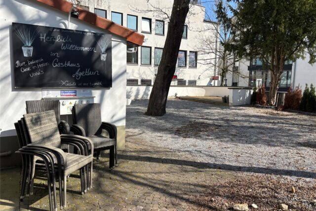 Gestapelte Stühle stehen in dem verwaisten Biergarten des Gasthauses Agethen in Unna. Auf einer großen Tafel werden Gäste willkommen geheißen.