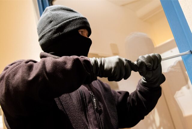Ein Einbrecher hebelt mit einem Stemmeisen ein Fenster auf.