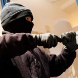 Ein Einbrecher hebelt mit einem Stemmeisen ein Fenster auf.