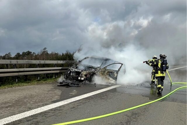 Zwei Feuerwehrleute löschen ein Fahrzeug auf der A1 bei Wermelskirchen. Es steht auf dem Seitenstreifen, eine Rauchwolke breitet sich aus.