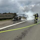 Zwei Feuerwehrleute löschen ein Fahrzeug auf der A1 bei Wermelskirchen. Es steht auf dem Seitenstreifen, eine Rauchwolke breitet sich aus.