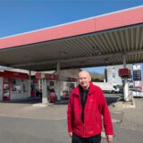 Ein Betreiber in roter Fleecejacke steht vor dem Zapfsäulen-Dach seiner Tankstelle.