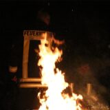 Ein Feuerwehrmann steht mit dem Rücken zu einer lodernden Flamme.