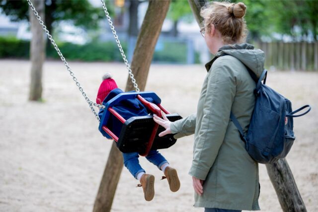 Ein Kind schaukelt, eine Frau schiebt es an.