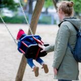 Ein Kind schaukelt, eine Frau schiebt es an.