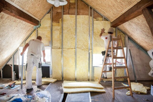 Zwei Handwerker dämmen das Dach eines Neubaus.