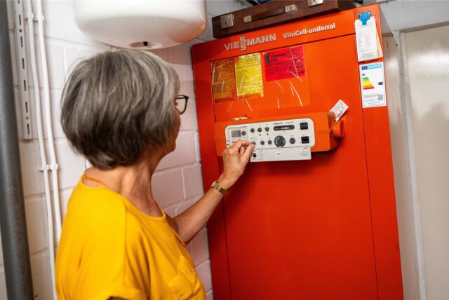 Eine Frau justiert die Steuerung eines Viessmann VitoCell-uniferral Heizkessels. Der Kessel trägt ein Energieeffizienzlabel der Klasse D.