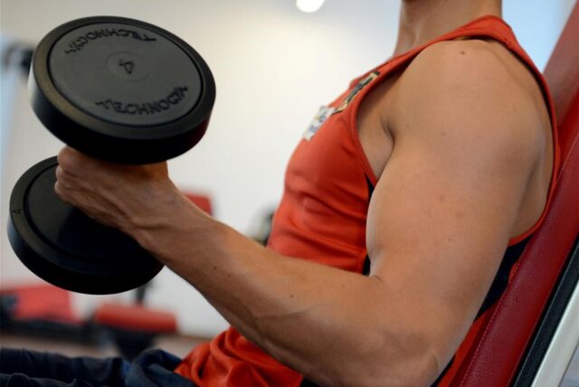 Ein Mann trainiert den Bizeps mit einer Hantel in einem Fitnessstudio.