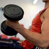 Ein Mann trainiert den Bizeps mit einer Hantel in einem Fitnessstudio.