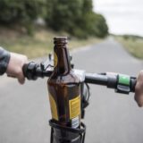 Ein Mann lenkt einen E-Scooter, in dessen Getränkehalterung eine Bierflasche steht.