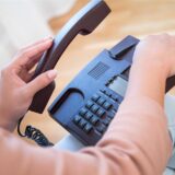Eine Frau hebt den Hörer ihres Telefons ab.