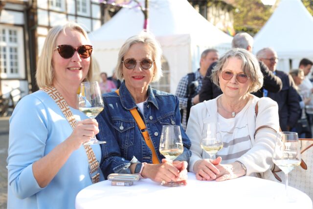 Drei Frauen stehen beim Genussfrühling in Werne an einem Stehtisch und trinken Weißwein.